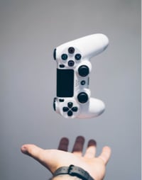 Photograph of a video game controller in the air above an open hand.